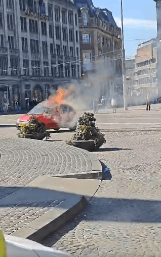 Car on fire in city square.