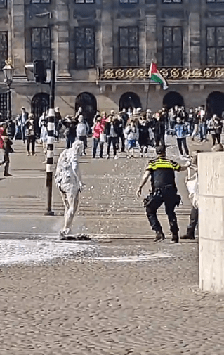 A person in white being sprayed with water by a police officer in front of a crowd.