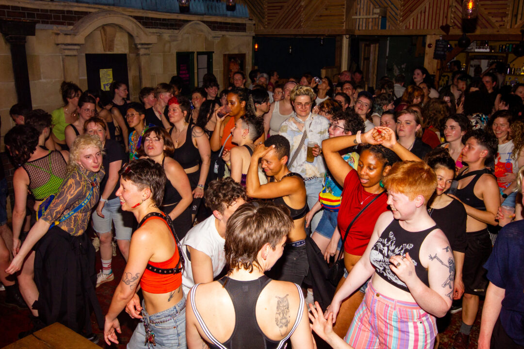 A large nightclub full of people dancing and smiling wearing all kinds of colourful outfits
