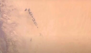 A group of military vehicles moving through a desert landscape, partially obscured by dense clouds of sand and dust.
