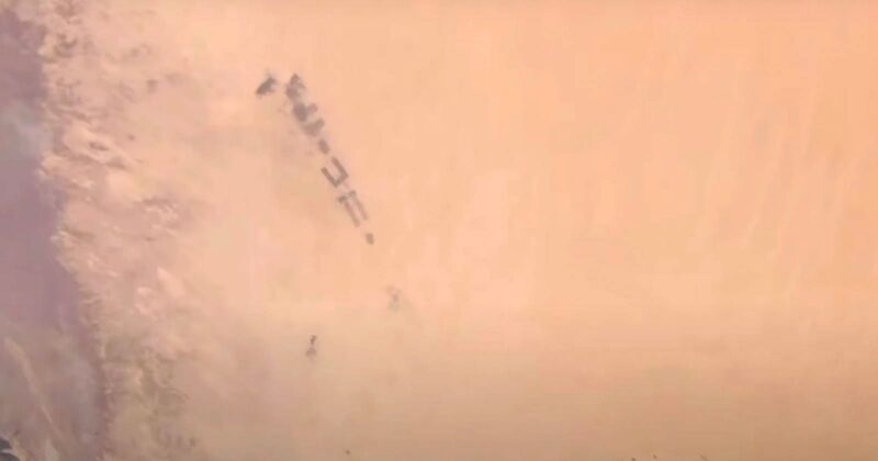 A group of military vehicles moving through a desert landscape, partially obscured by dense clouds of sand and dust.