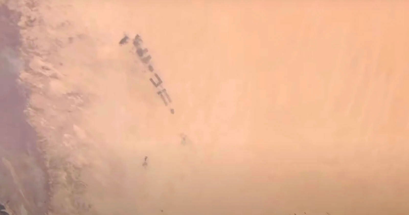 A group of military vehicles moving through a desert landscape, partially obscured by dense clouds of sand and dust.