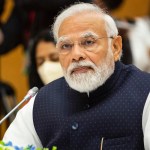 Portrait of Narendra Modi before a microphone.