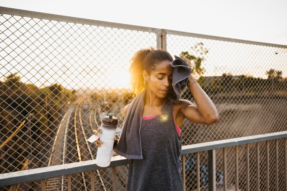 Healthy young woman wiping her sweat with a towel after training session. Exhausted fitness female resting after workout.