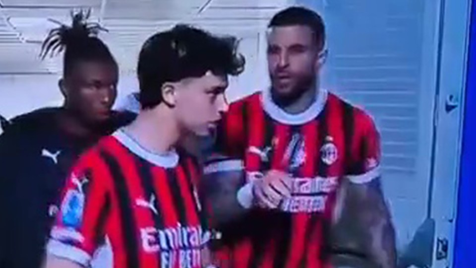 Two soccer players in AC Milan jerseys talking.