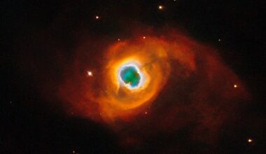 The image holds a planetary nebula, a glowing shell of material thrown off by a dying star. A glowing, jagged ring encircles a small central region of greenish clouds, making it appear like a hole torn in fabric. This “hole” is itself encircled by a band of silvery-blue clouds and a larger, fainter, yellow ring of gas. Puffy, smoky clouds of orange and red gas billow out from there into a large oval nebula, fading into the dark background of space dotted by stars.