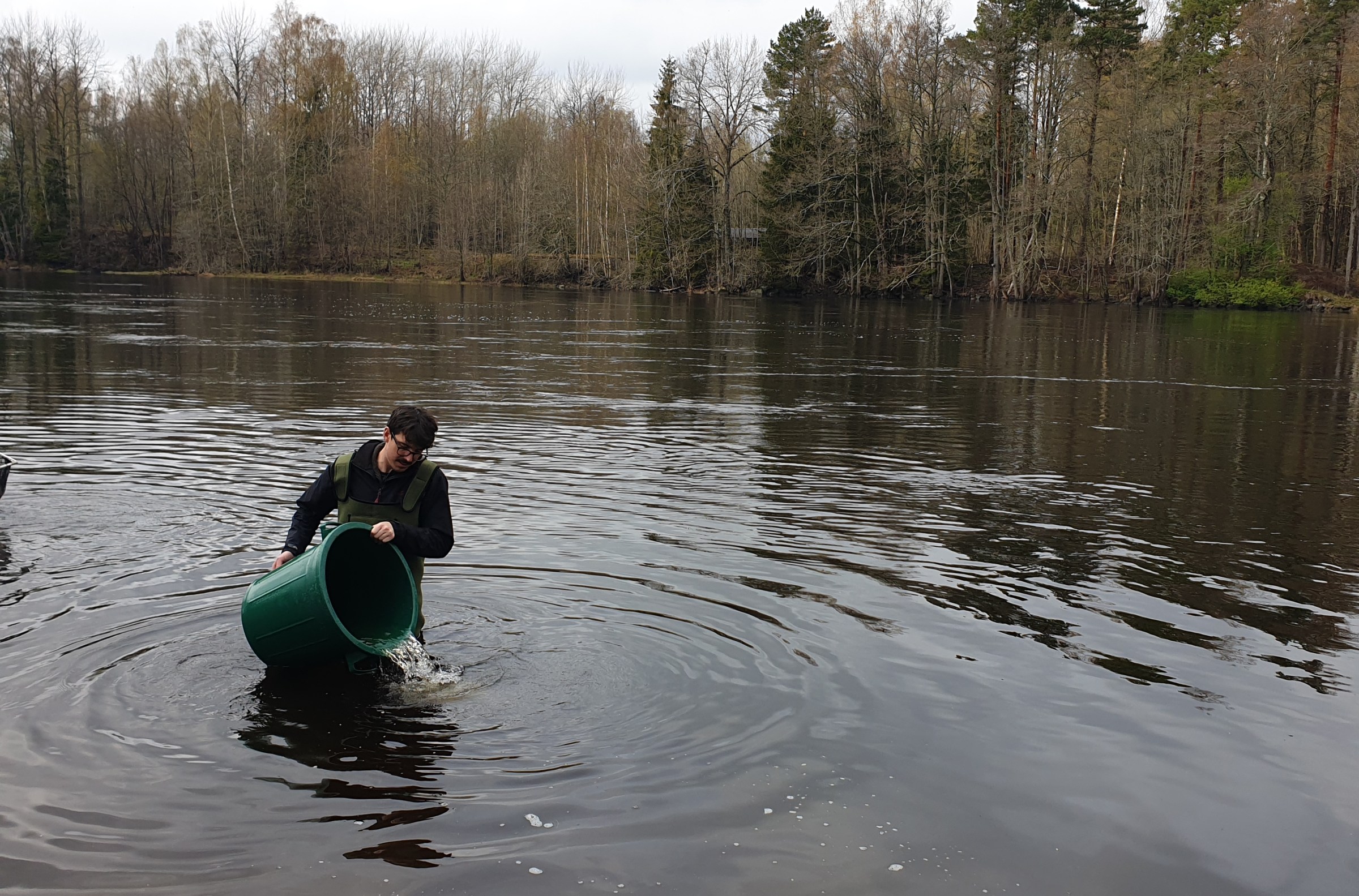 A man in the water pouring out a bucket of water.