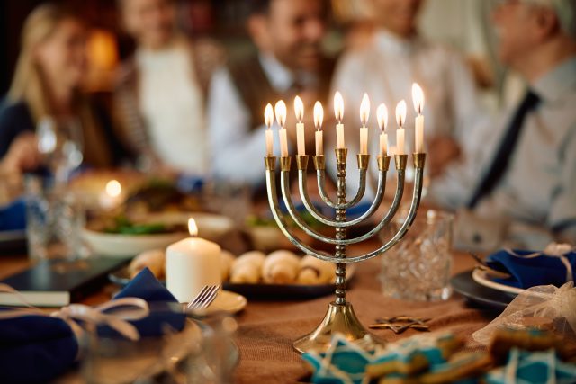 Lit menorah with multigeneration family in the background during Hanukkah celebration.