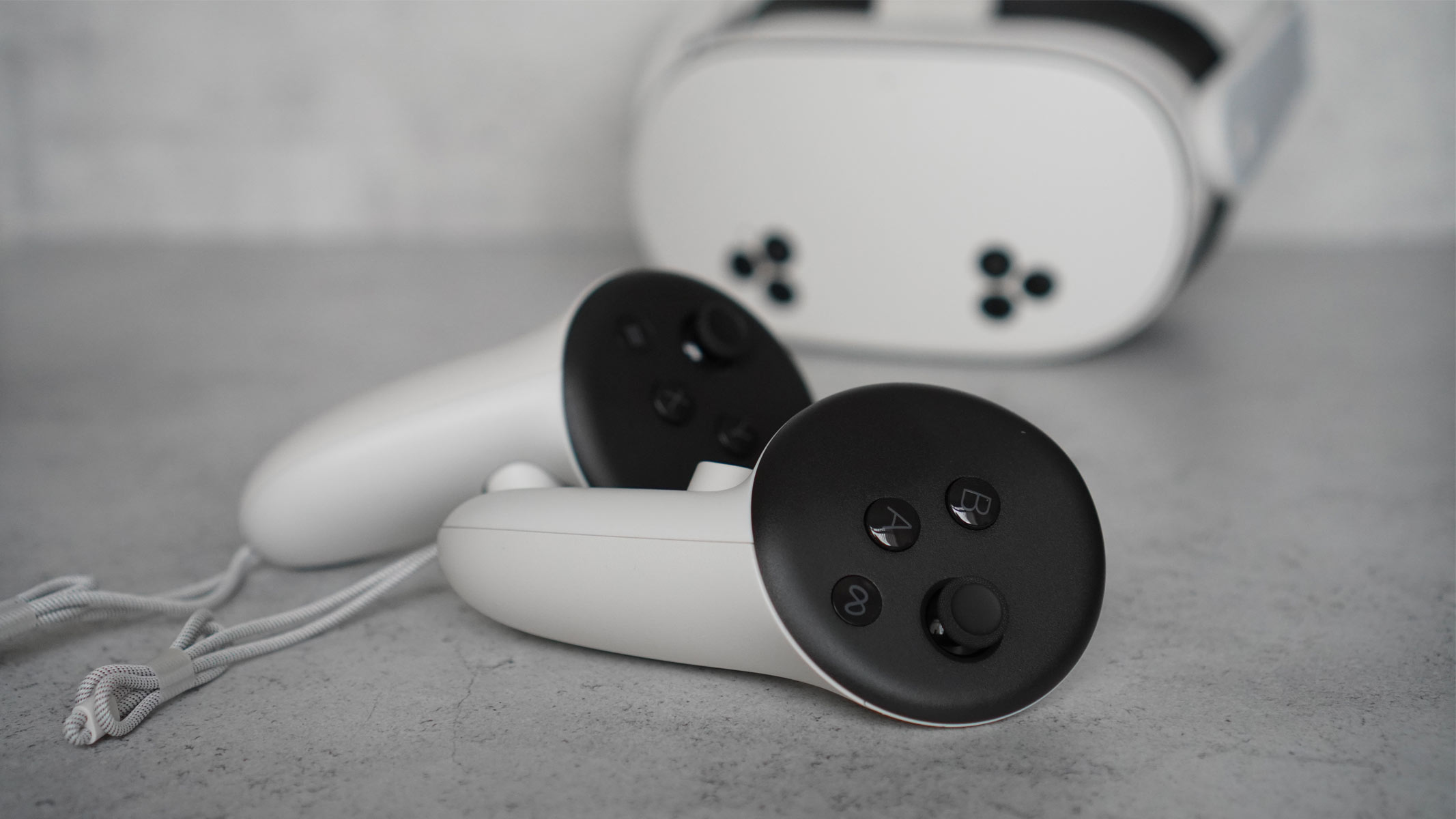 The Meta Quest 3S is a white headset with black cameras on the front and white controllers on a gray background