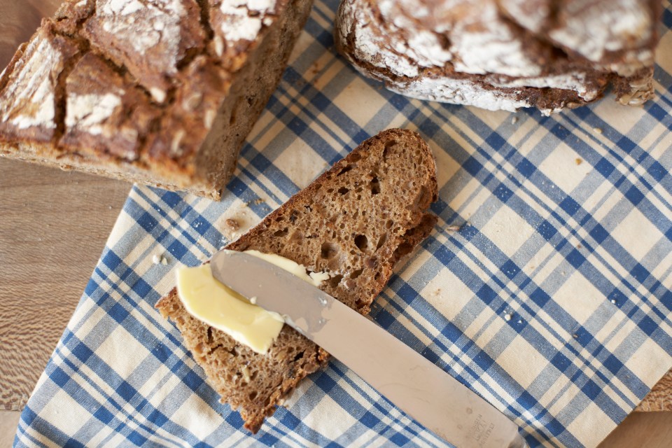 Slice of 7-grain bread with butter being spread on it.