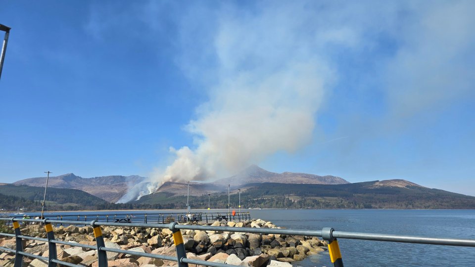 Smoke from a hillside fire over a body of water.