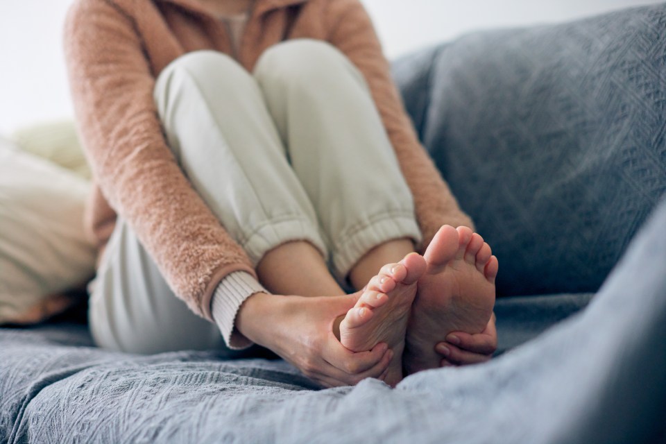 Woman massaging her feet while sitting on a couch.