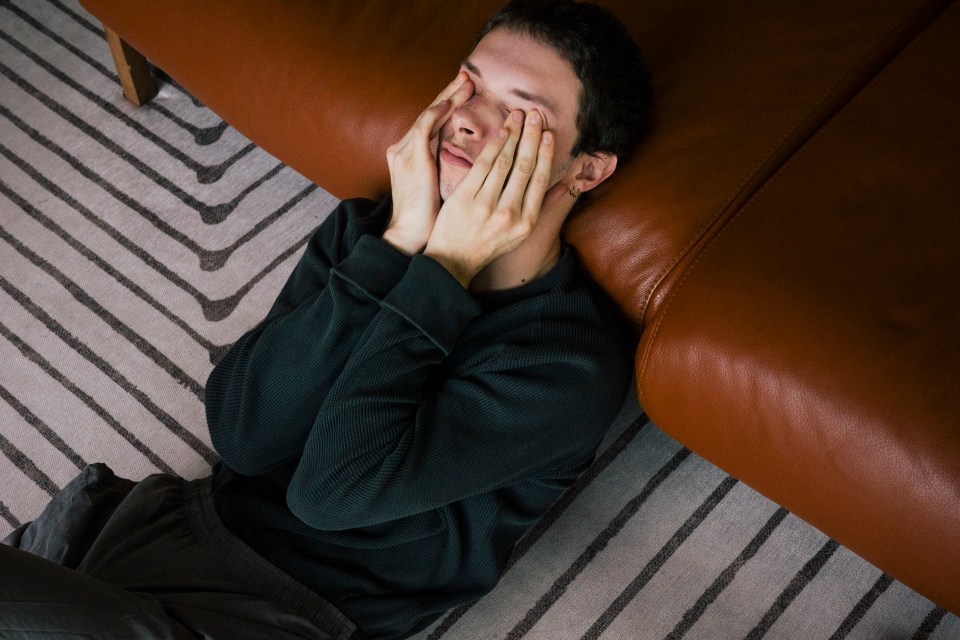 A young man sits on the floor, head in his hands, appearing distressed.