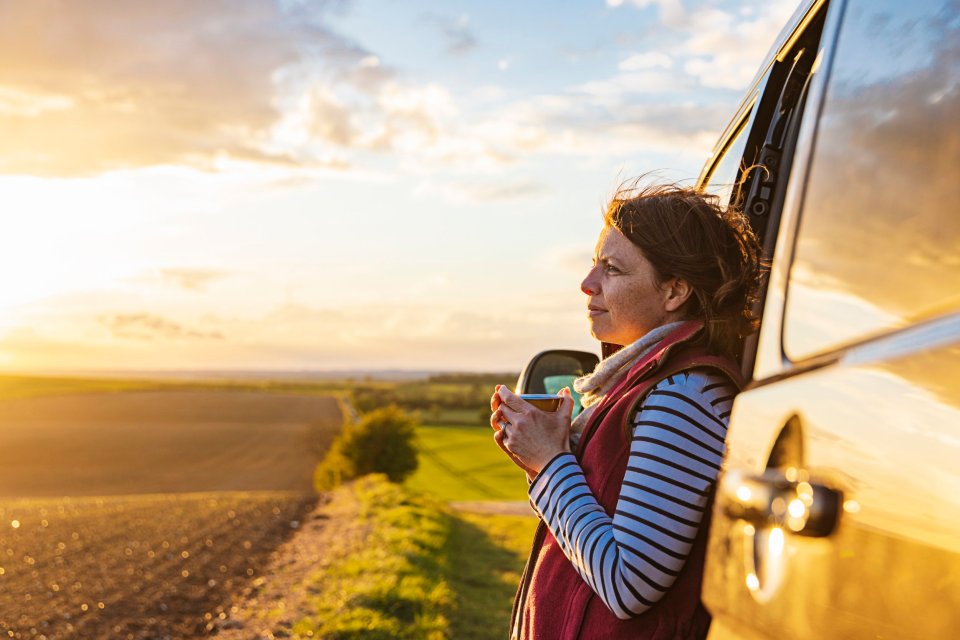 Woman enjoying a hot drink while looking at a sunset view from her campervan.