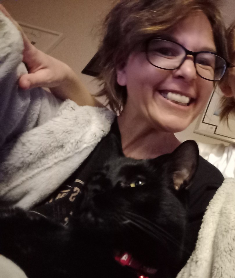 Woman smiling and holding a black cat.