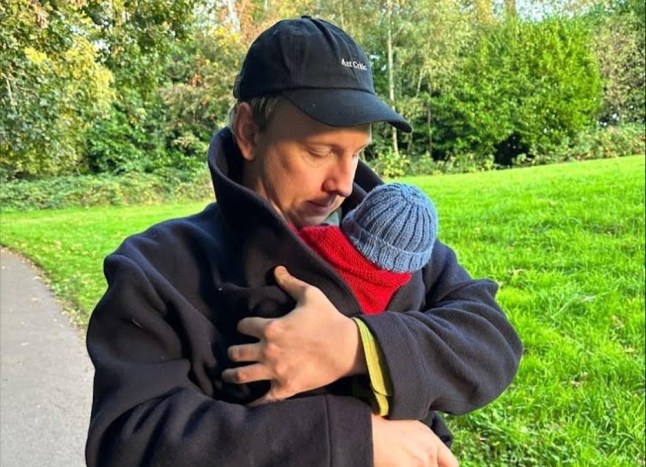 Joe Lycett wrapping his infant son in his coat to keep him warm.