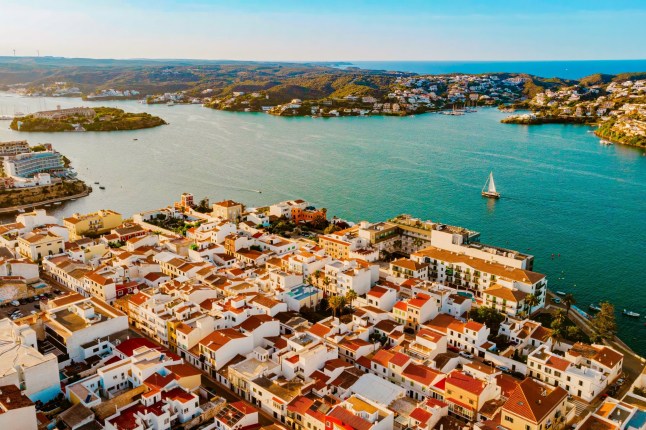 An aerial view of Es Castell on the Menorca coast, looking over orange-roofed buildings and the sea.