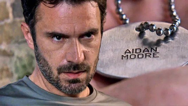John Sugden looking menacing next to dog tags with 'Aidan Moore' engraved on them in Emmerdale