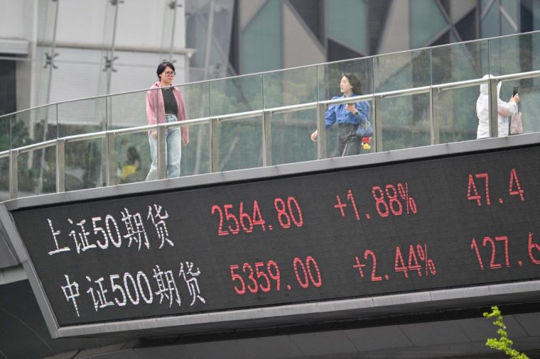 People walk across a foot bridge showing a screen displaying financial markets information at the financial district in Shanghai on April 9, 2025. US President Donald Trump forged ahead with tariffs of over 100 percent against Chinese goods after Beijing refused to withdraw its retaliation as the world's biggest economies go head-to-head in a ruinous trade war that has rocked global markets. (Photo by Hector RETAMAL / AFP) (Photo by HECTOR RETAMAL/AFP via Getty Images)