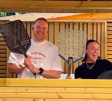 Colson Smith and Ellie Leach pose in a garden holding pizza peels