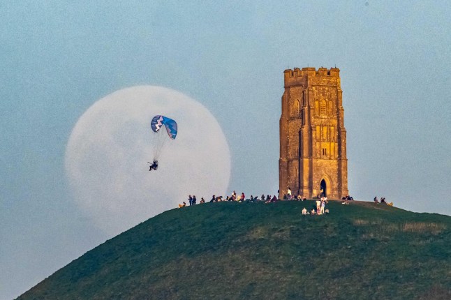 Alamy Live News. 3AK4WGJ Glastonbury, Somerset, UK. 11th April 2025. UK Weather. A paramotor flies in front of the almost full Pink moon as it rises up from behind St Michael?s Tower on Glastonbury Tor in Somerset as a crowd of people gather on top of the hill to watch. Picture Credit: Graham Hunt/Alamy Live News This is an Alamy Live News image and may not be part of your current Alamy deal . If you are unsure, please contact our sales team to check.