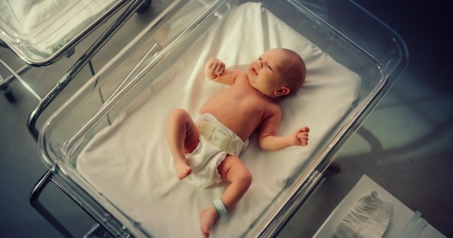 A newborn baby pictured from above laying in a hospital bed in a maternity unit.
