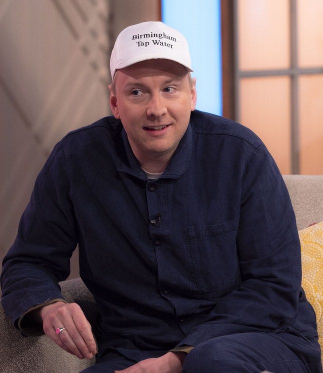 Joe Lycett listens to Lorraine Kelly while wearing a white base ball cap