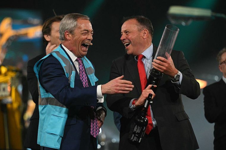 TOPSHOT - Reform UK Leader Nigel Farage (L) reacts as Reform UK Mayoral Candidate Arron Banks fires blue hi-vis jackets into the audience during the political party's Local Election Campaign Launch, in Birmingham, central England, on March 28, 2025. (Photo by Oli SCARFF / AFP) (Photo by OLI SCARFF/AFP via Getty Images)