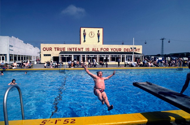 Man falling backwards into swimming pool in Butlins holiday camp, Skegness. The slogan 'Our true intent is all for your delight' was borrowed from Midsummers Night's Dream. Butlins Skegness is a holiday camp located in Ingoldmells near Skegness in Lincolnshire. Sir William Butlin conceived of its creation based on his experiences at a Canadian summer camp in his youth and by observation of the actions of other holiday accommodation providers, both in seaside resort lodging houses and in earlier smaller holiday campsThe camp began opened in 1936, when it quickly proved to be a success with a need for expansion. The camp included dining and recreation facilities, such as dance halls and sports fields. Over the past 75 years the camp has seen continuous use and development, in the mid-1980s and again in the late 1990s being subject to substantial investment and redevelopment. In the late 1990s the site was re-branded as a holiday resort, and remains open today as one of three remaining Butlins resorts. (photo by Barry/In Pictures via Getty Images Images)