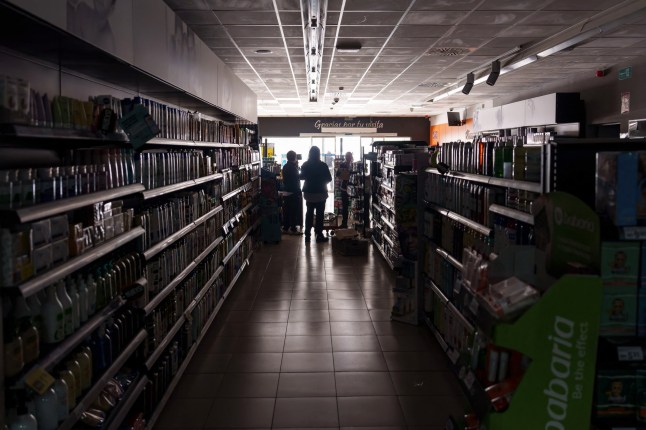 Employees stand inside a supermarket without lights in Burgos on April 28, 2025, during a massive power cut affecting the entire Iberian peninsula and the south of France. A 