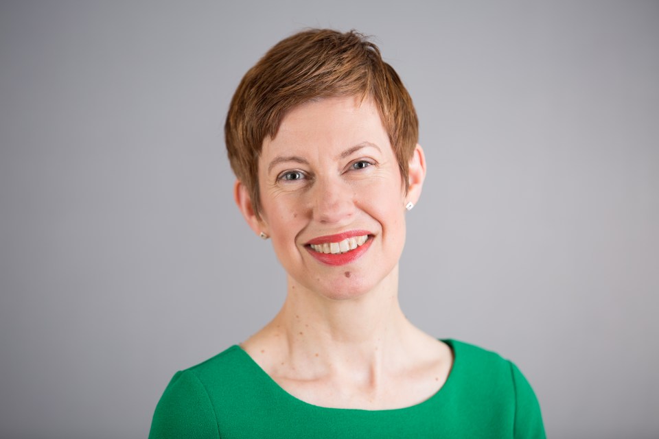 Portrait of a smiling woman with short brown hair wearing a green dress.