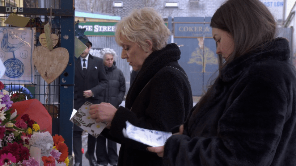 Two women reading cards at a memorial with flowers.