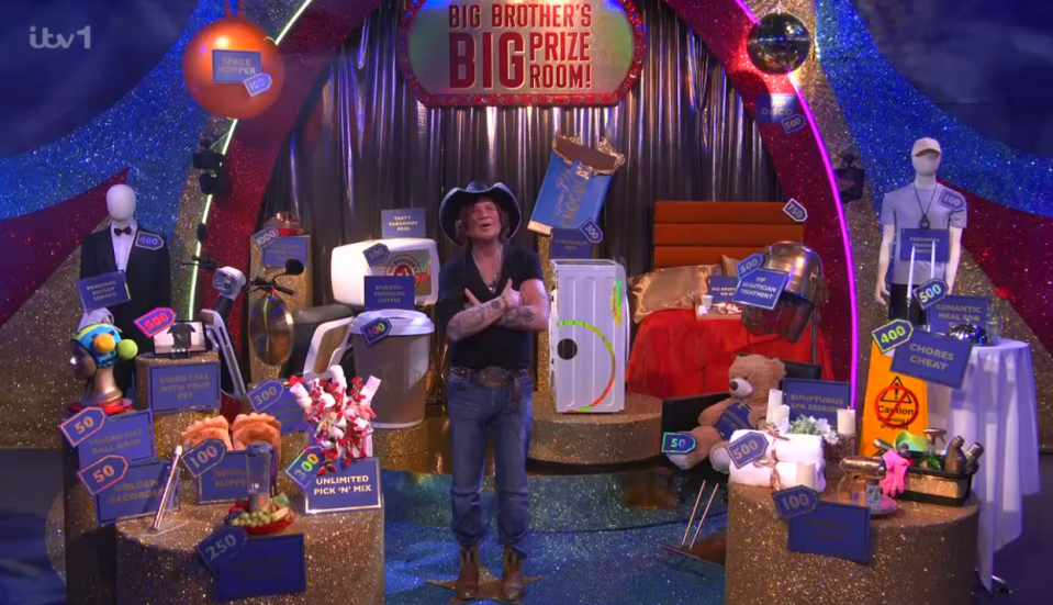 Screenshot of a man standing in a room filled with prizes and price tags for Big Brother's Big Prize Room.