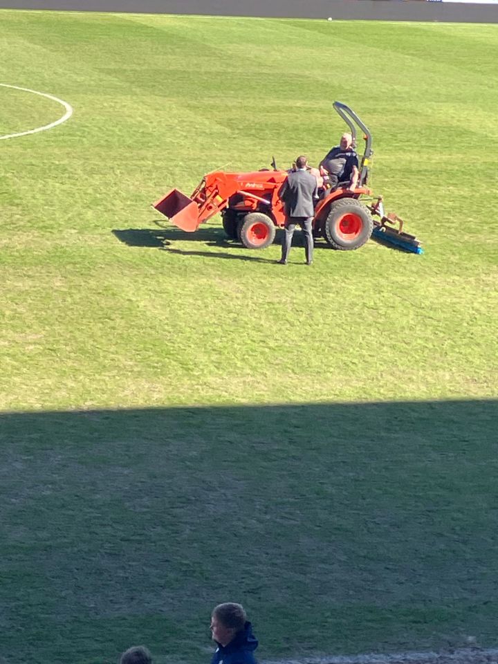 Three men on a small tractor on a soccer field.