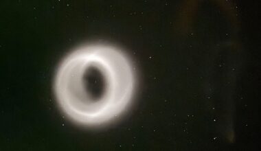 A glowing, ring-shaped phenomenon appears in the night sky, surrounded by scattered stars. The ring emits a soft white light, creating a striking contrast against the dark background.