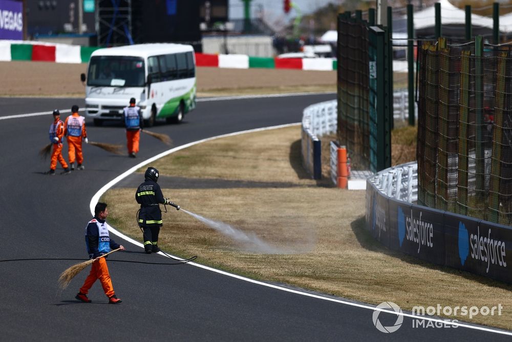 A fire fighter sprays the grass at the side of the track to dampen it after fires during final practice