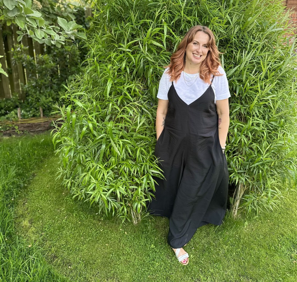 Woman in black jumpsuit standing in a garden.