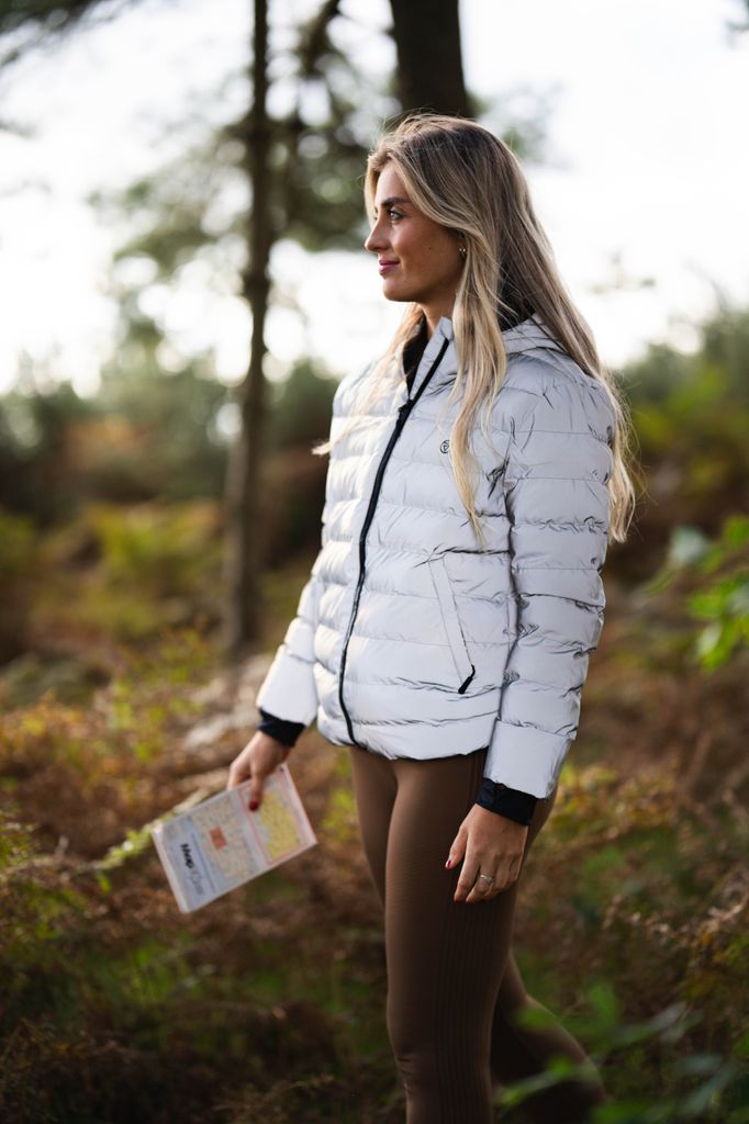 Woman in a reflective silver coat smiling as she heads out on a hike 