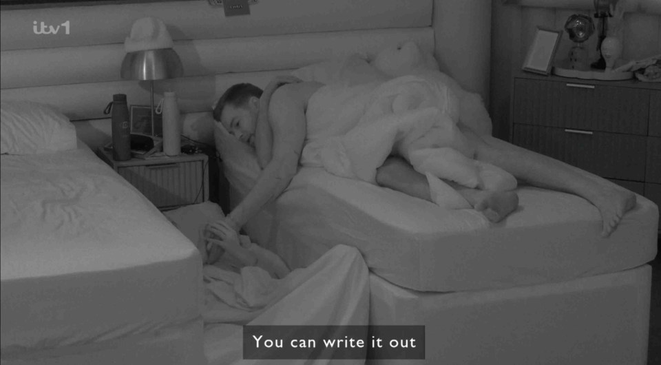 Black and white photo of a person writing on another person's hand while they sleep.