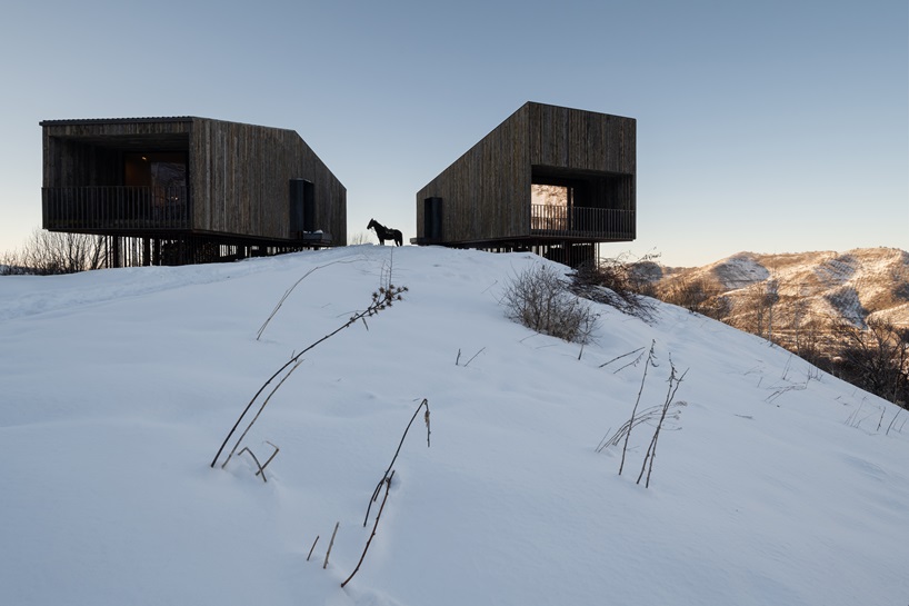 reclaimed dark larchwood clads aum cabins' facades amid mountainscape in kazakhstan