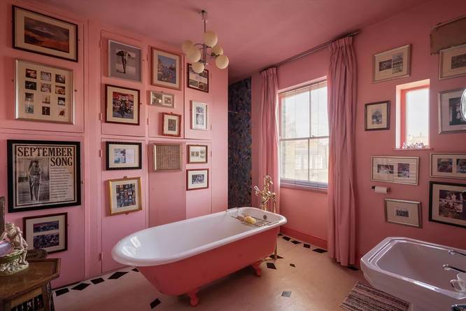 A free standing bathtub inside a bathroom with pink walls covered in framed photos
