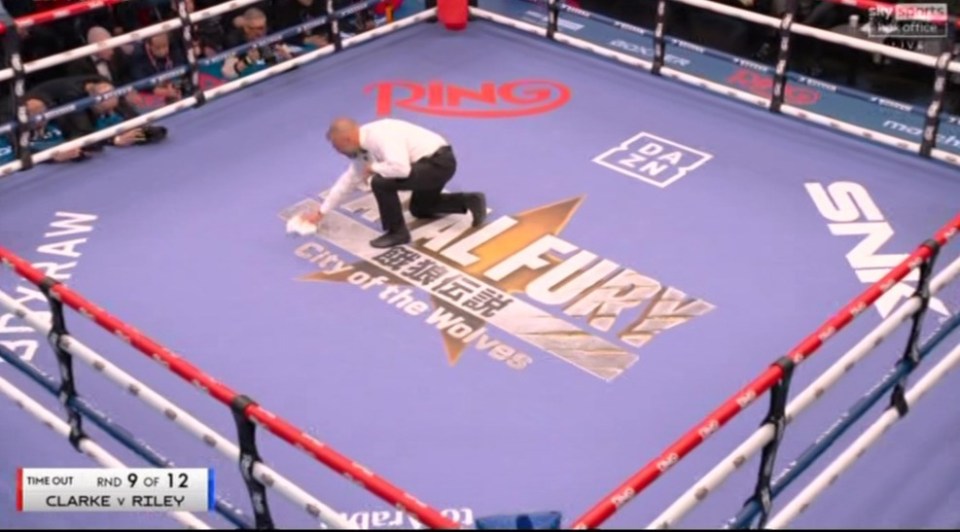 A boxing ring official cleaning the boxing ring canvas.