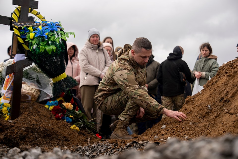 A soldier touches the soil at a funeral ceremony.