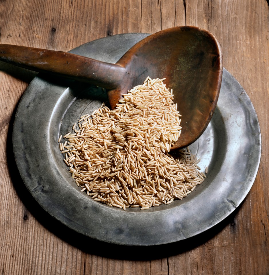 Brown rice in a metal bowl with a wooden spoon.