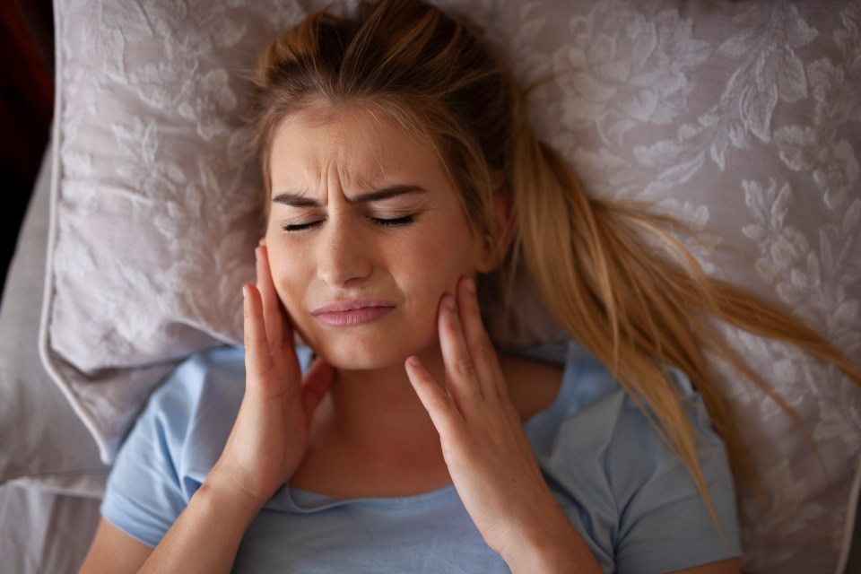 Woman in bed holding her jaw, experiencing bruxism.