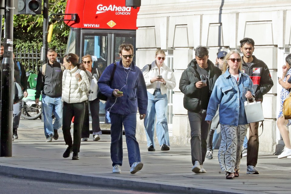 Harry Styles walking down a London street with a mustache.