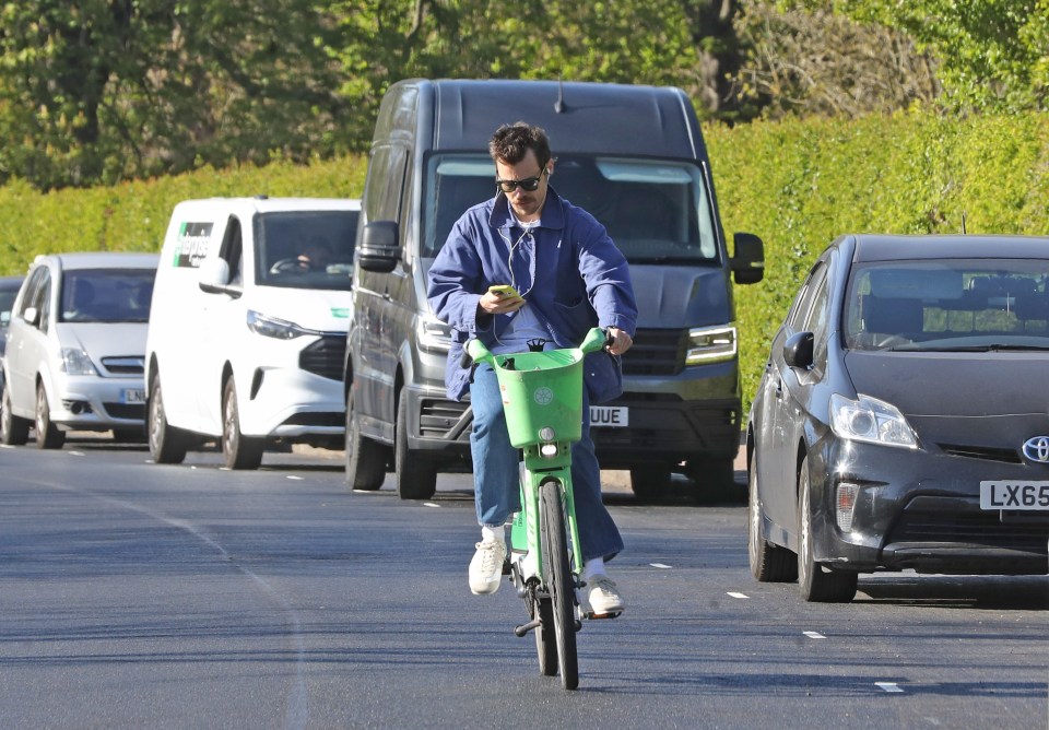Harry Styles riding a lime green bike while looking at his phone.