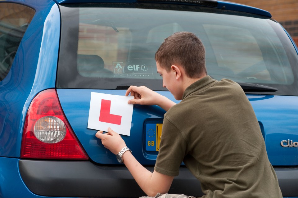 Teenage boy placing an L-plate on the back of a car.