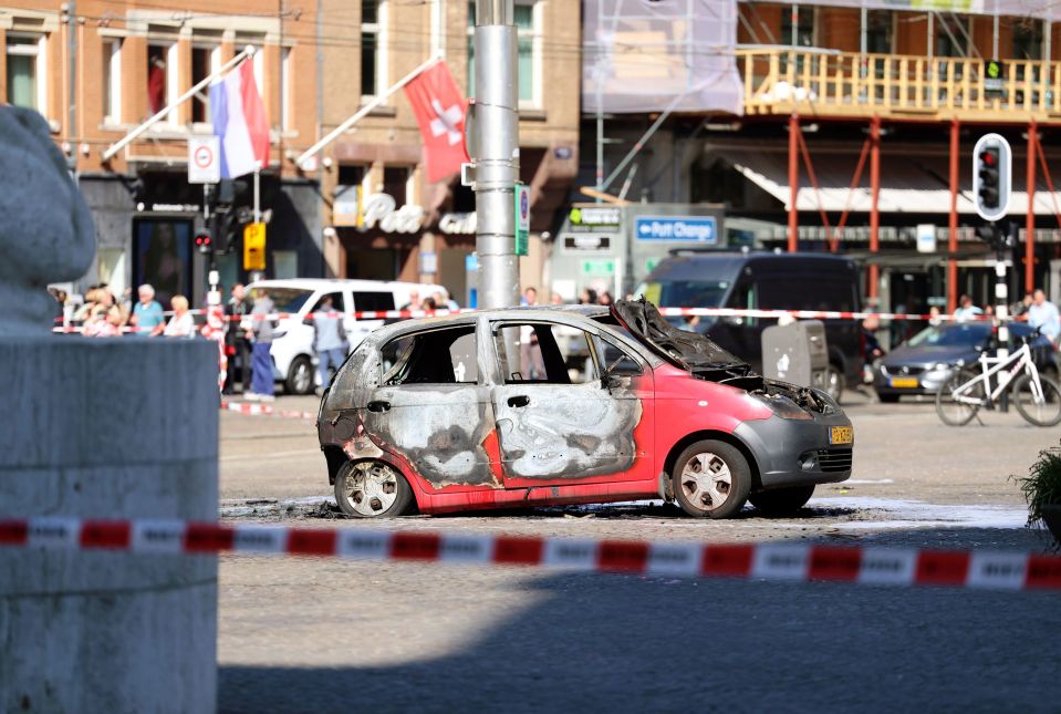 Burned-out car on Dam Square near a monument.