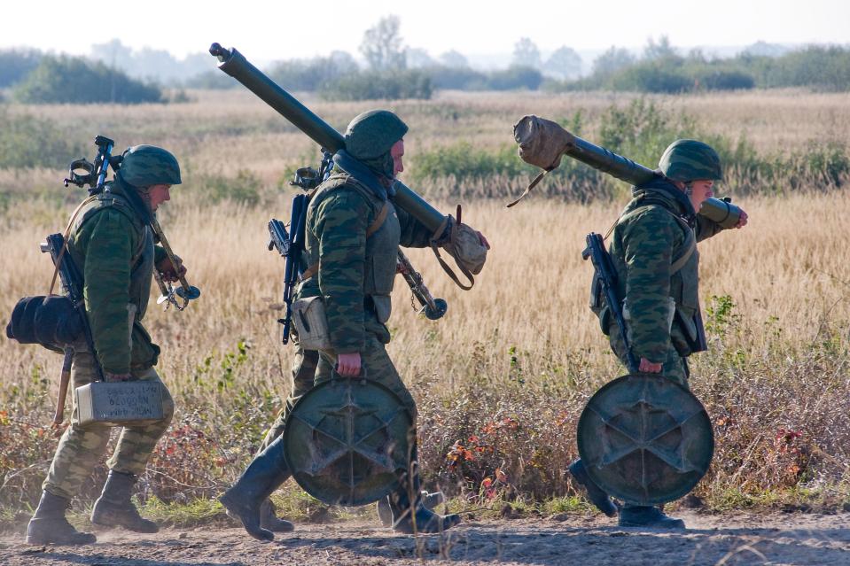 Three soldiers carrying mortars and other equipment during a military exercise.